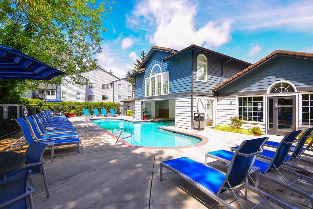 a swimming pool with blue chairs in front of a house