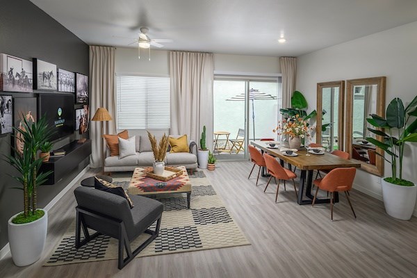 A modern living room with a grey sofa, a wooden dining table, and a ceiling fan.