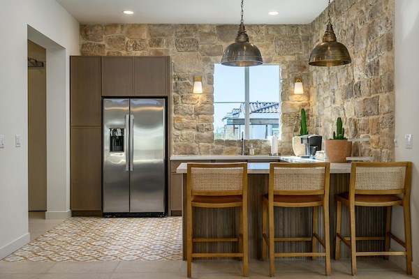 A kitchen with a stone wall and a stainless steel refrigerator.