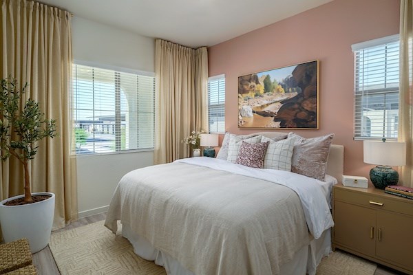 A bedroom with a large bed, a potted plant, and a painting on the wall.
