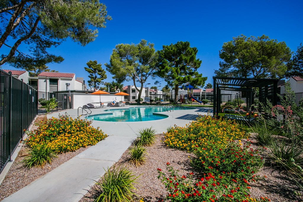 a pool is surrounded by flowers and trees and a fence