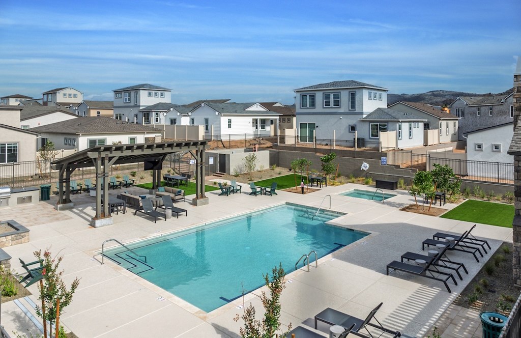 A large swimming pool surrounded by a patio with lounge chairs and a pavilion.