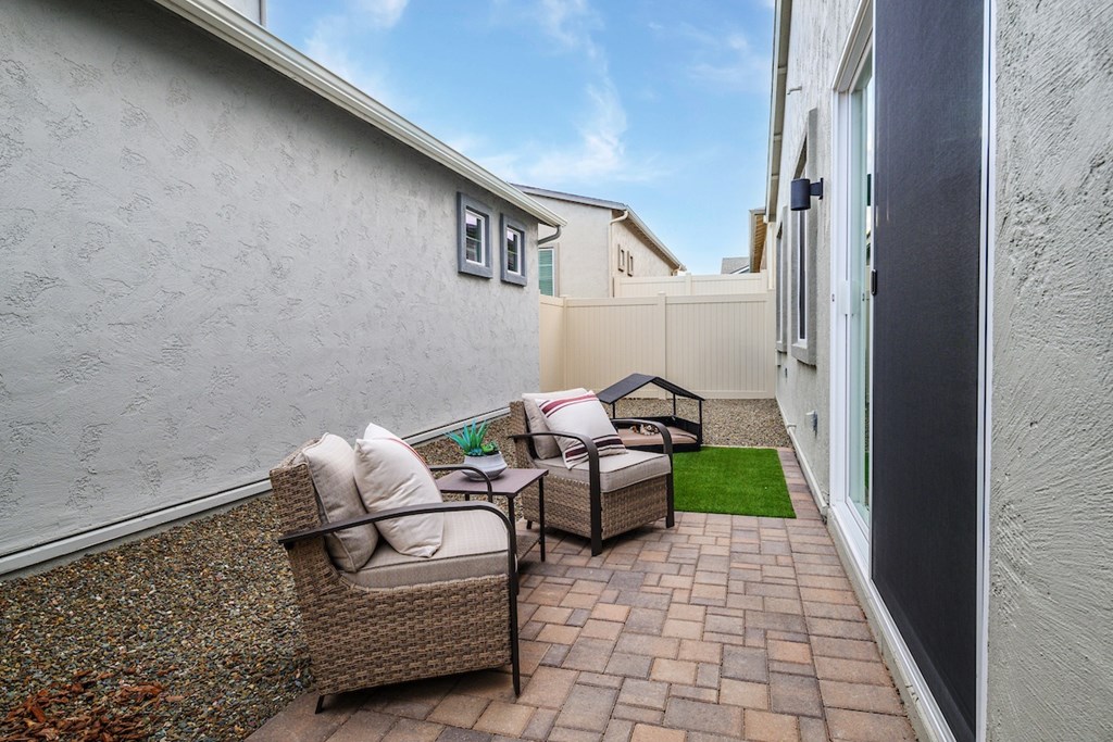 A patio with a wicker chair and a table with a red and white striped cushion.