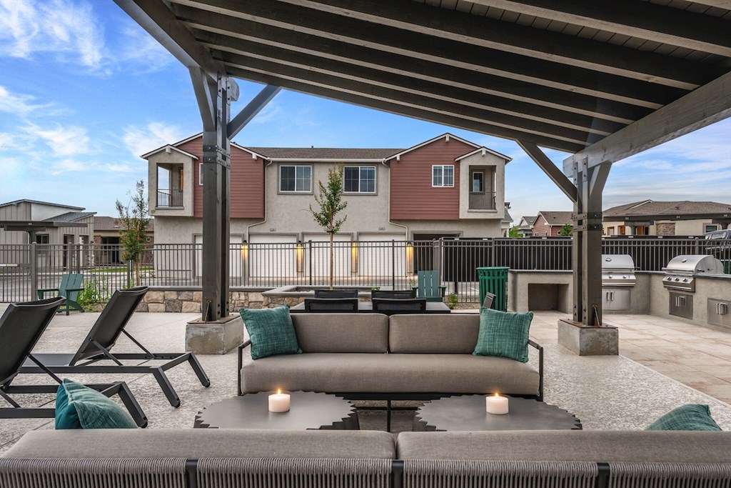 A patio with a couch, chairs, and candles under a roof.