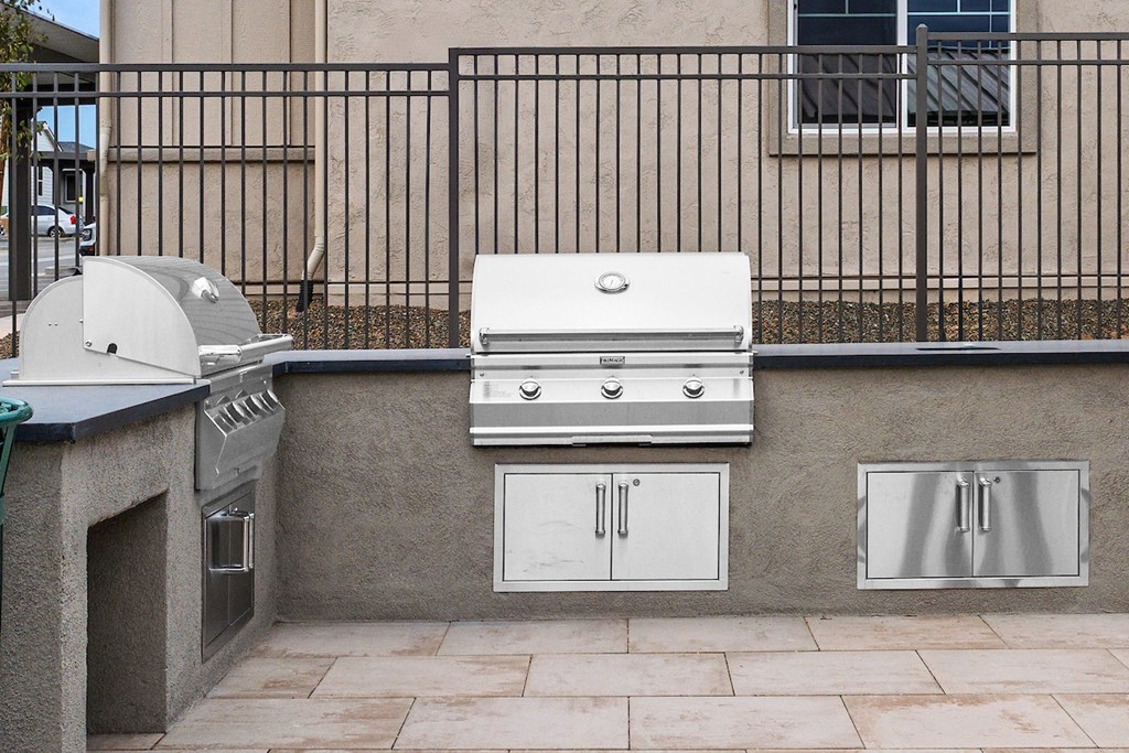 A white grill is on a patio next to a wall and a window.