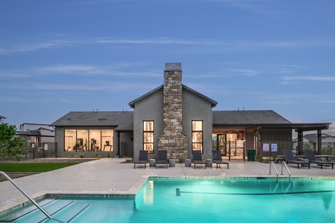 A modern house with a stone chimney and a pool in front.