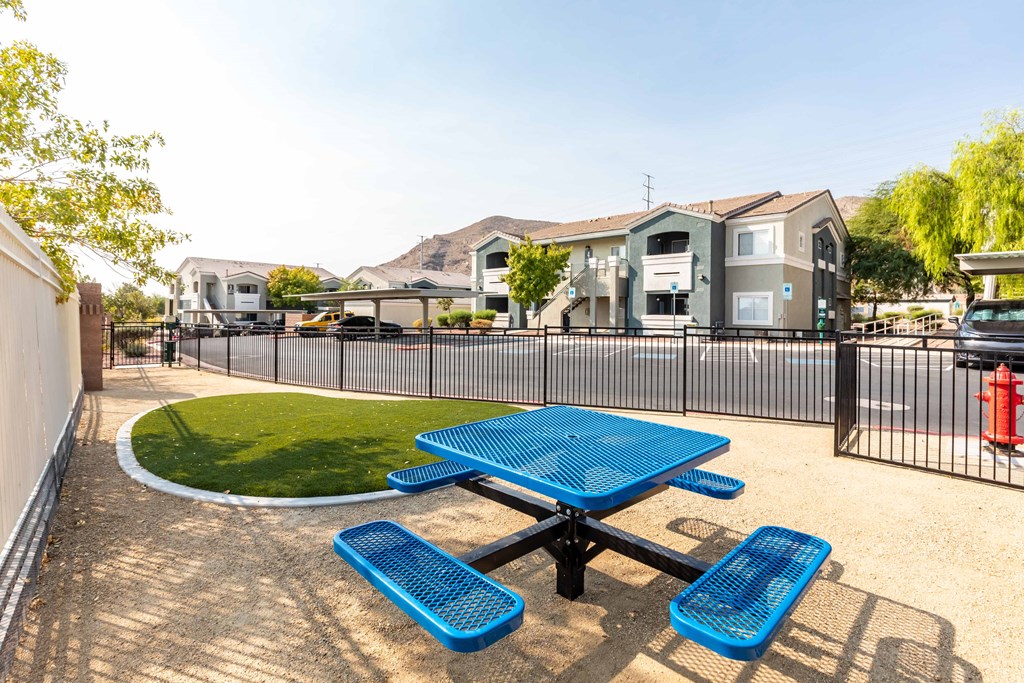 a picnic table with blue benches in a fenced in area with apartment buildings