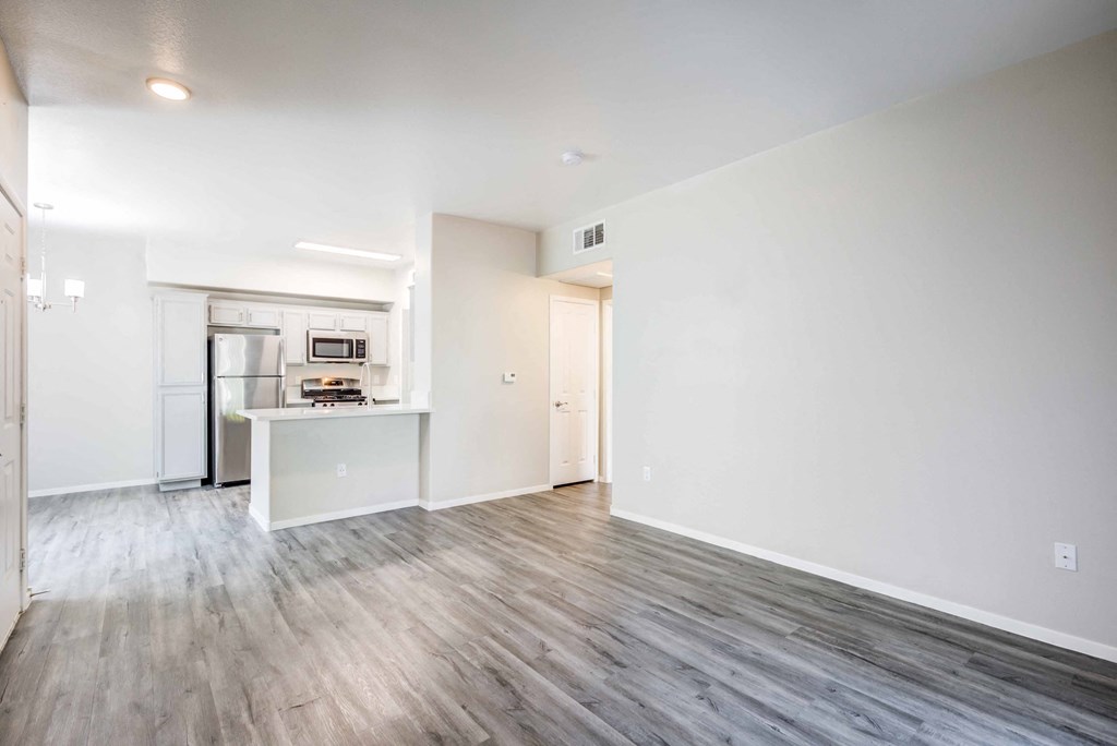 the living room and kitchen of an apartment with white walls and wood floors