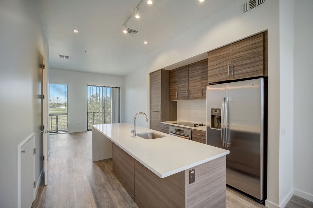 2-Bedroom Apartments in Scottsdale, AZ - Dusk Scottsdale - Gourmet Kitchen with Wood-Style Flooring, Stainless Steel Appliances, White Quartz Countertops, Cooking Island, Modern Custom-Wood Cabinetry, Overhead Lighting, and View of Living Room.