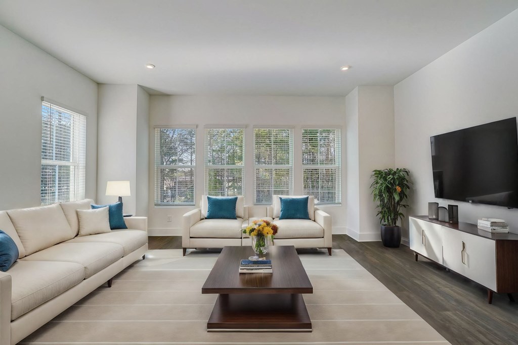 Pet-friendly townhome living room with white couches, coffee table, hardwood floors, and large windows at Henley Avondale in Avondale Estates, GA.