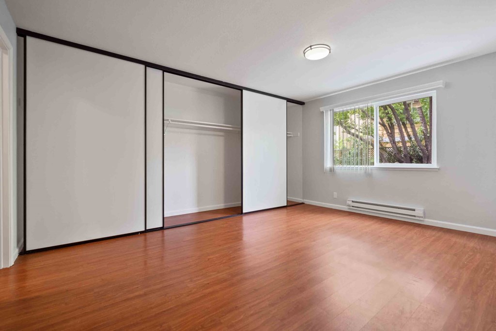 Two Bedroom Apartments in Santa Clara, CA - Hidden Lake - Spacious Bedroom with Wood-Style Flooring, Grey Walls, Large Window, and Sliding Closet Doors