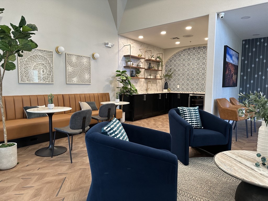 a lounge area with blue chairs and tables and a kitchen in the background