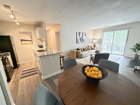 A kitchen area with a refrigerator, a dining table with chairs, and a bowl of oranges on the table.