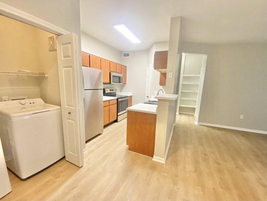 A kitchen and living room with wooden floor and stainless steel appliances and wood cabinets.