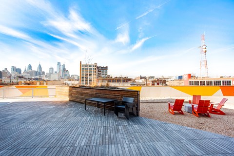 A wooden bench with black cushions is in the foreground of a rooftop with a city skyline in the background.