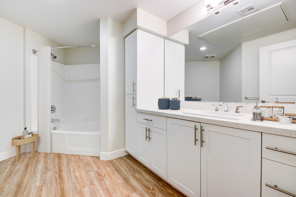A white bathroom with a wooden floor and a white bathtub.