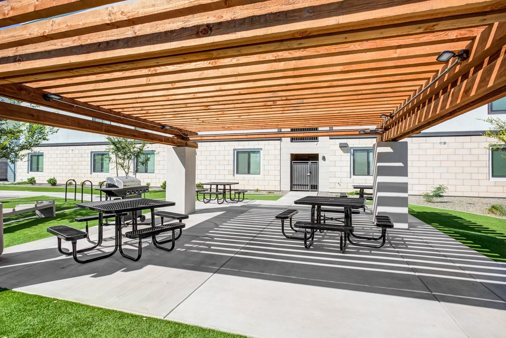 Modern Studio Apartments in Phoenix, AZ - Imperial Apartments - Outdoor BBQ Area under Pergola with Picnic Tables, BBQ Grill, and Surrounding Grassy Area.