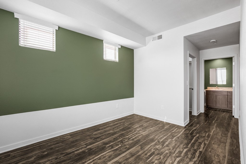 Apartments in Downtown Phoenix, AZ - Imperial Apartments - Spacious Empty Bedroom with Wood-Style Flooring, Green Accent Wall with Windows, and Access to Oversized Closet and Bathroom.