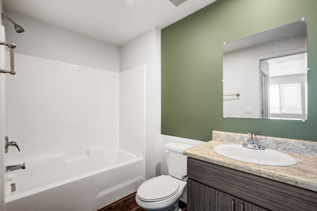 Apartments Downtown Phoenix - Imperial Apartments - Bathroom with Green Accent Wall, Shower and Bathtub Combo with White Tile Backsplash, Wood-Style Flooring, Vanity with Sink and Mirror.