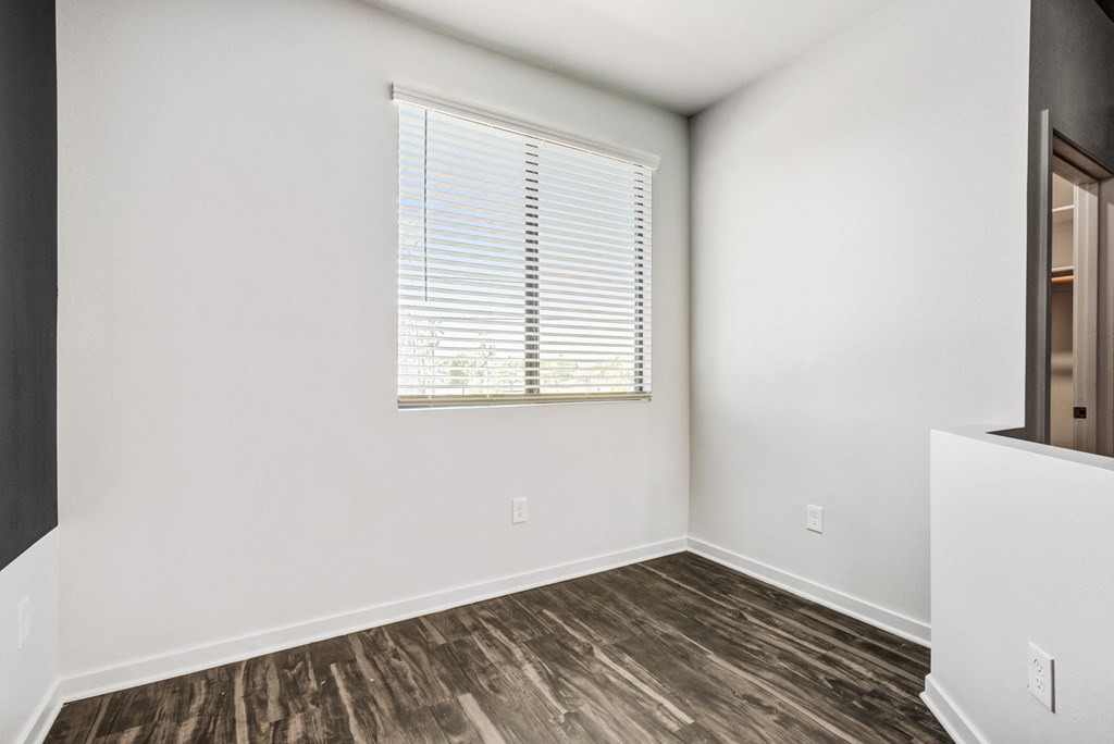 Apartments in Downtown Phoenix, AZ - Imperial - Den Area with Wood-Style Flooring, White Walls, and a Large Window.