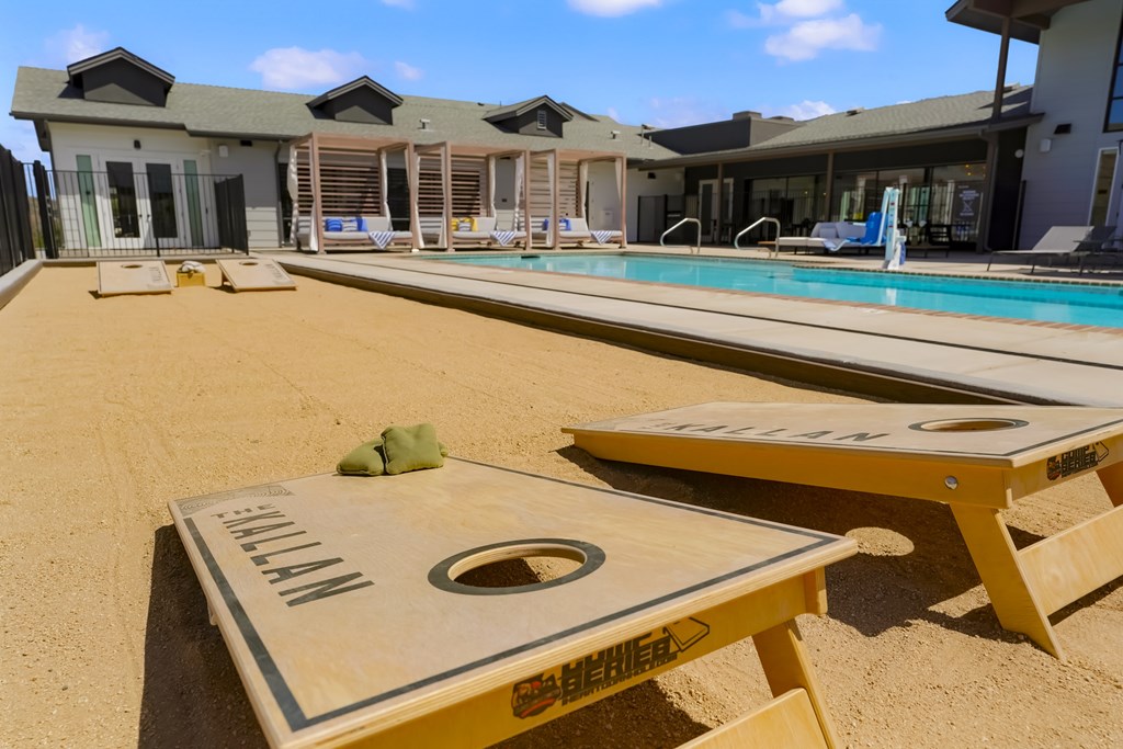 A sand volleyball court is in the foreground of a resort with a pool and lounging area in the background.