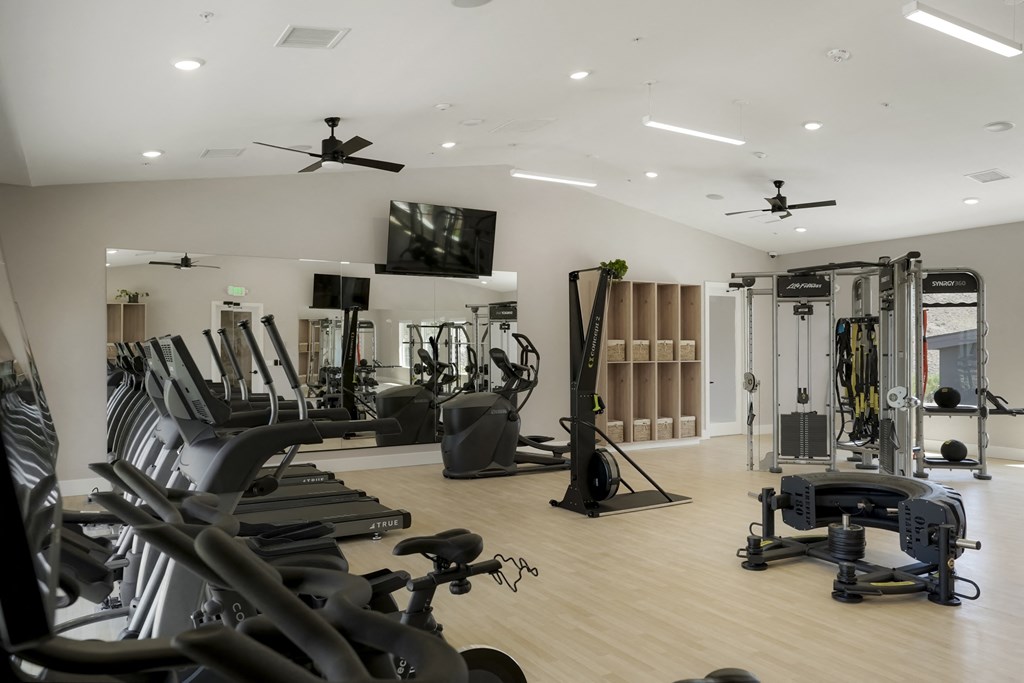 a gym with cardio equipment and weights on a wooden floor