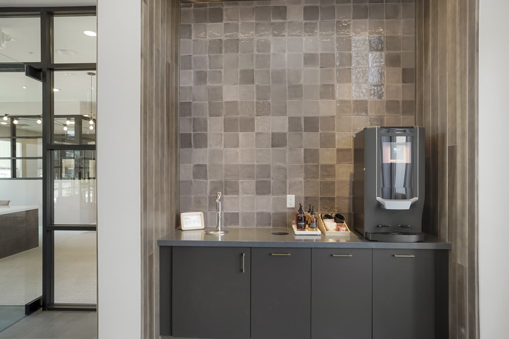 A kitchen with a grey cabinet and a grey and white tiled wall.