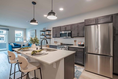 2-Bedroom Luxury Apartments in Kenosha, WI - Karrick - Modern Kitchen With Luxury Wood Vinyl Flooring, Island Seating, Quartz Countertops, Stainless Steel Appliances, And Pendant Lighting.