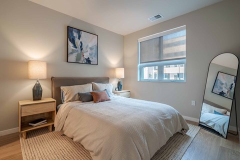 A bedroom with a large bed, a nightstand with a lamp, and a painting on the wall.