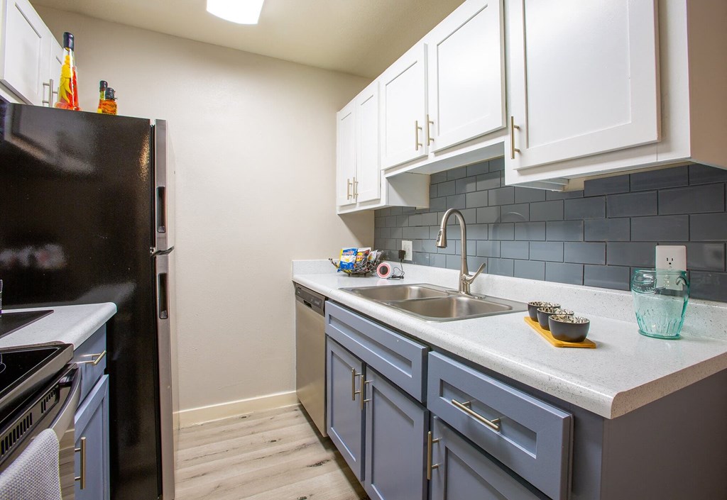 One-BR Apartments in Tucson, AZ - Peaks at Redington - Kitchen with Black and Stainless Steel Appliances, Blue and White Cabinets, Blue Tile Backsplash, and Wood-Style Flooring