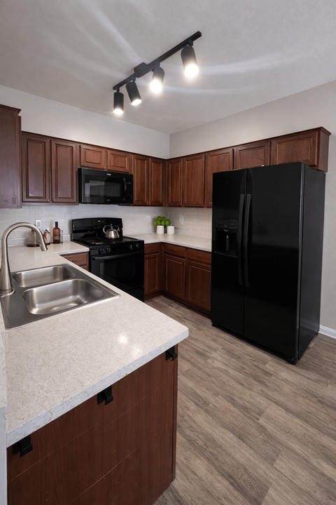 A kitchen with a black refrigerator and brown cabinets.
