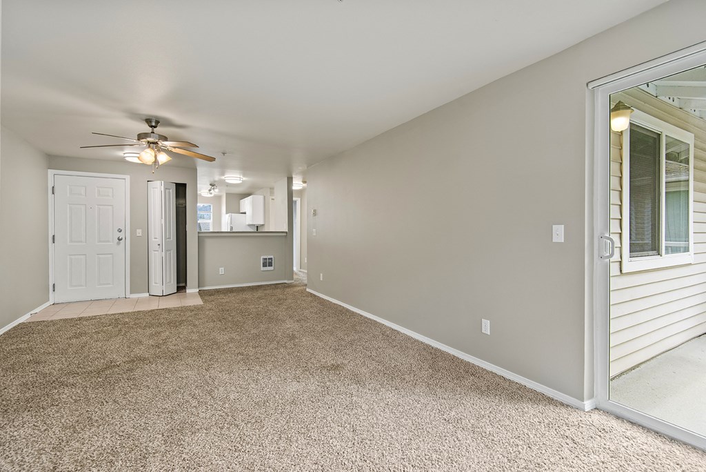 an empty living room with a ceiling fan and a door to a kitchen