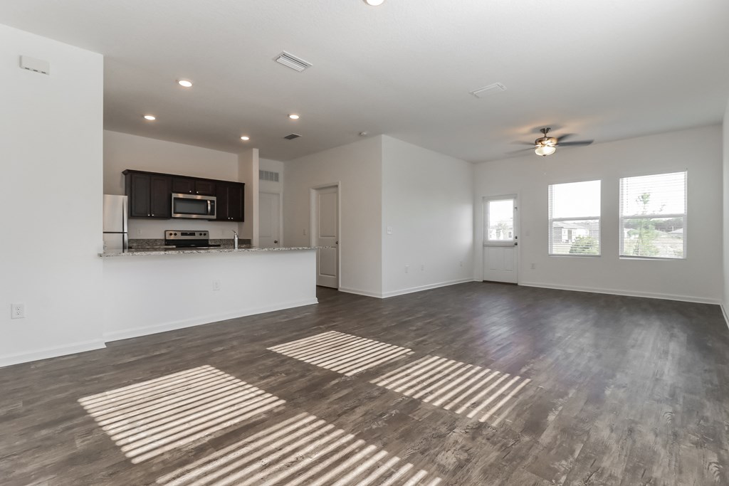 A spacious living room with a kitchen area in the background.
