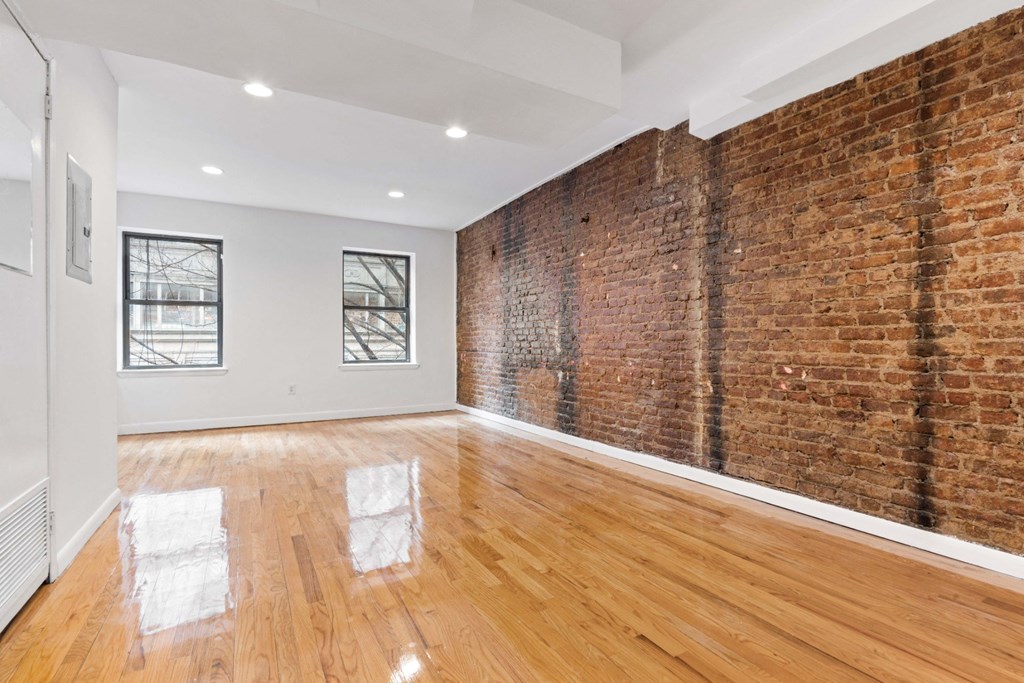 an empty living room with a brick wall and wooden floors