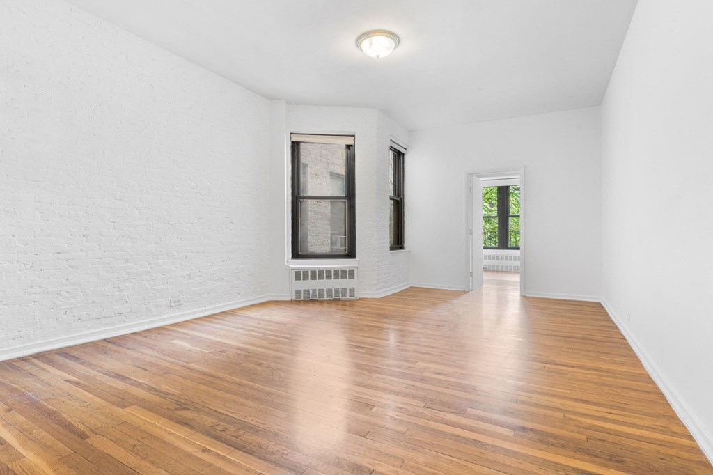 a living room with white walls and wood floors and a window