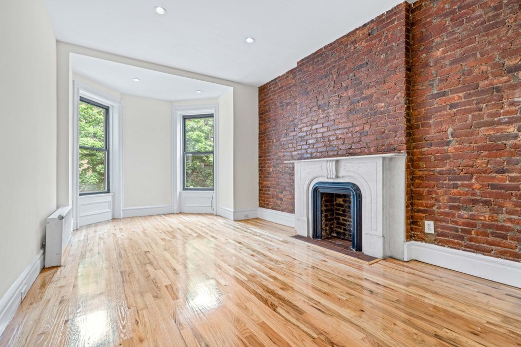 an empty living room with a brick fireplace and wooden floors