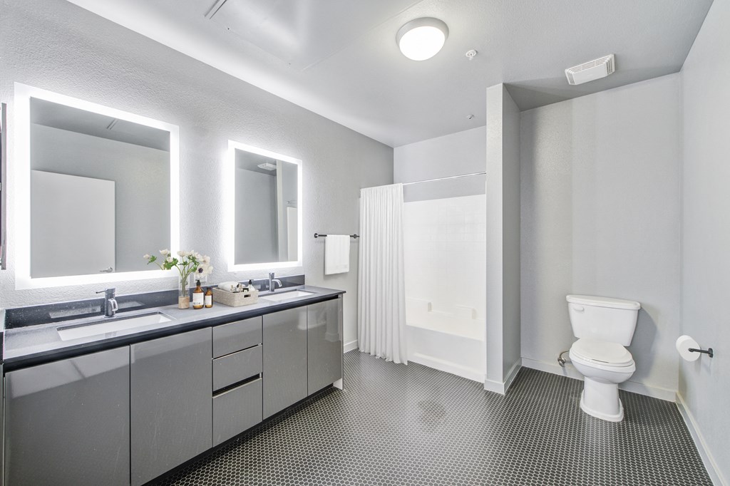 North Hollywood CA Apartments - Lofts at NoHo Commons - Large Bathroom with Shower and Tub, Toilet, Double-Sinked Vanity, Steel Gray Cabinets, Tiled Floor, and Mirrors with Lighting