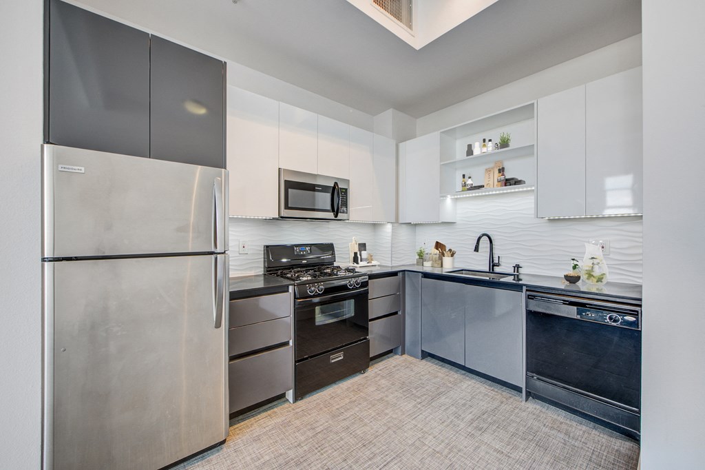 Lofts in North Hollywood CA - Lofts at NoHo Commons - Bright Kitchen with Stainless Steel and Black Appliances, White and Grey Cabinetry, Storage Space, Grey Countertops, and Textured Backsplash