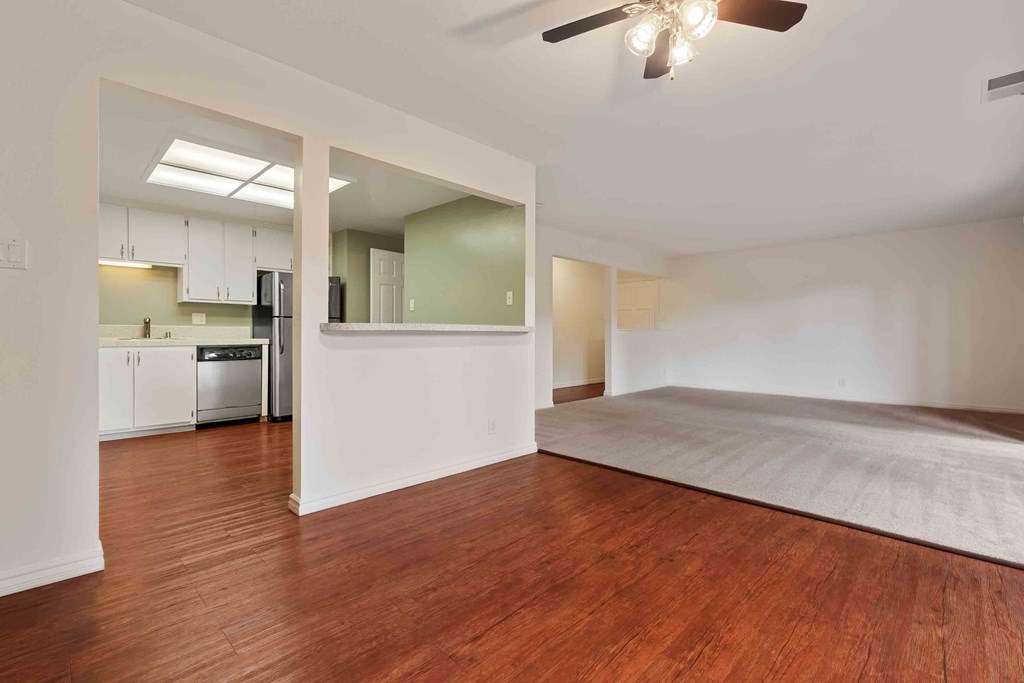 an empty living room and kitchen with wood floors and a ceiling fan