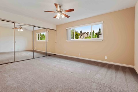 Three-Bedroom Apartments in Fremont, CA - Logan Park Apartments - Bright Bedroom With Mirrored Closet Doors, Soft Carpet, Ceiling Fan, and Wide Window.
