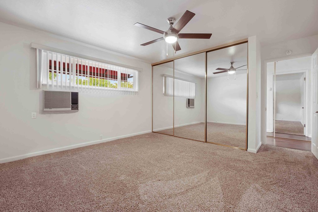 1 Bedroom Apartments In San Lorenzo, CA - Lorenzo Commons - Spacious Bedroom With Carpet Flooring, A Closet With Mirror Doors, A Ceiling Fan, A Window, And An A/C Unit