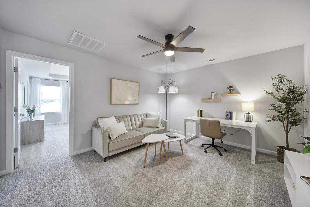 A living room with a couch, a chair, a desk, and a ceiling fan.