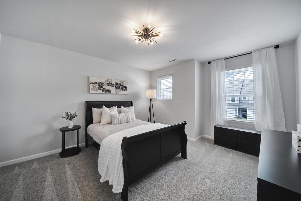 A bedroom with a large bed and a window with white curtains.