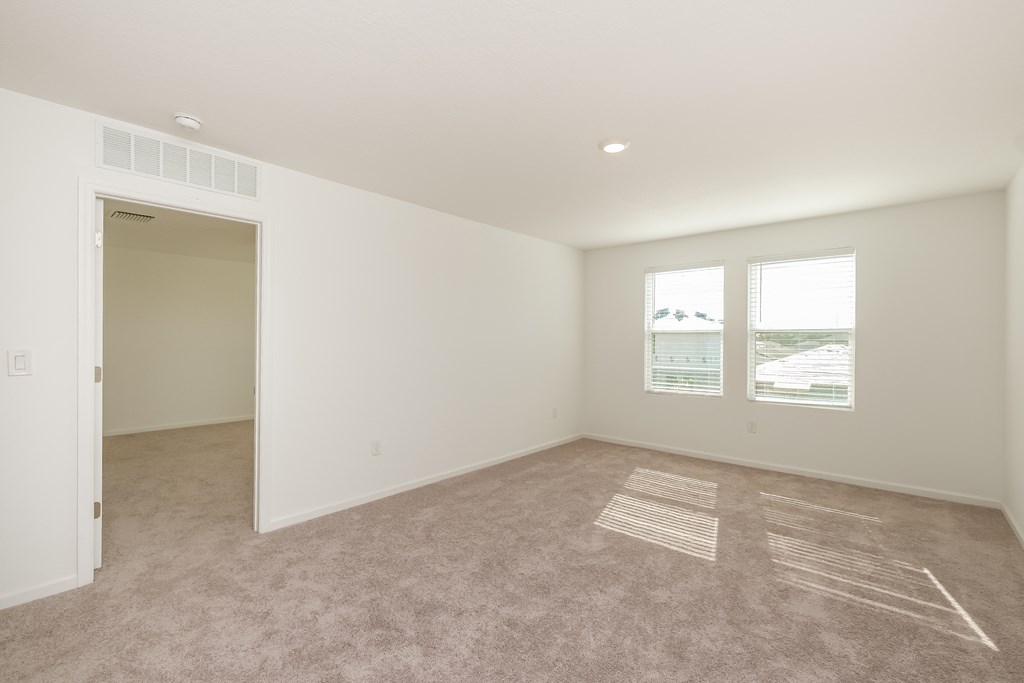 A large empty room with a carpet on the floor and a window showing a view of the outside.