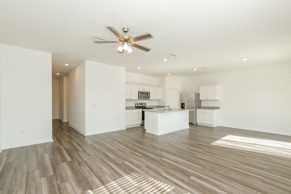 A spacious kitchen and living room with a ceiling fan and lighting.