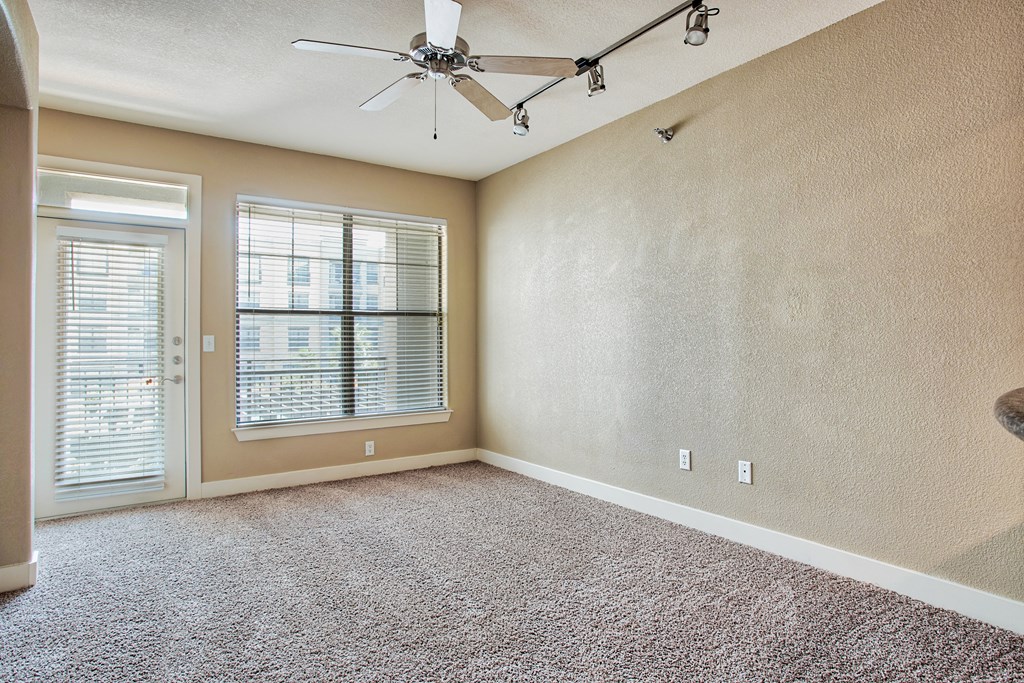 A living room with carpet floors and ceiling fan and lights and glass door and windows with blinds
