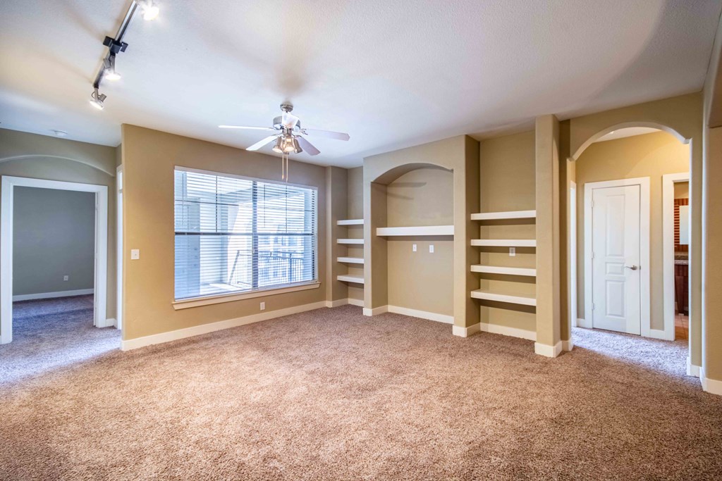 a living room with carpet floors and shelves and ceiling fan and ceiling lights and doors