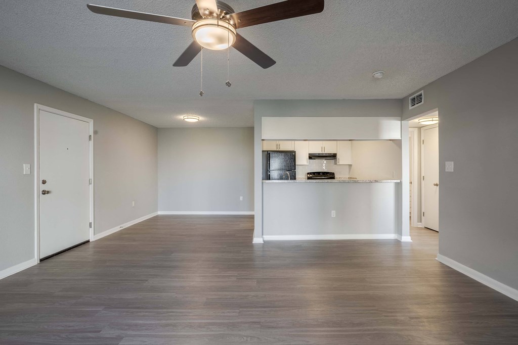 A room with a ceiling fan and a kitchenette in the background.
