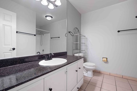 Dog-Friendly Apartments in Gilroy, CA - Mission Park - Clean Bathroom With Long Single-Sink Vanity, Oversized Wall Mirror, Granite-Look Countertop, Tub-Shower Combo, and Tile Flooring.