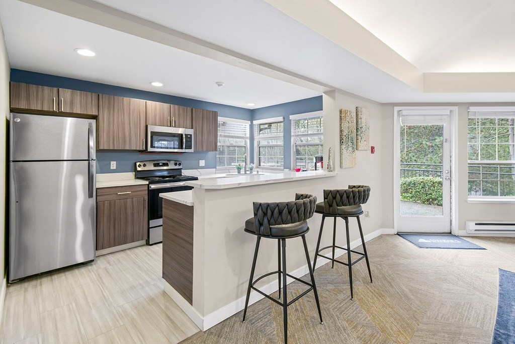 A kitchen with a refrigerator, stove, and bar stools.